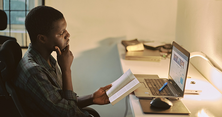 Man sitting at a desk with an open book and laptop