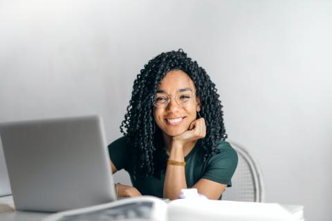 Woman sitting in chair at table staring at laptop screen and smiling